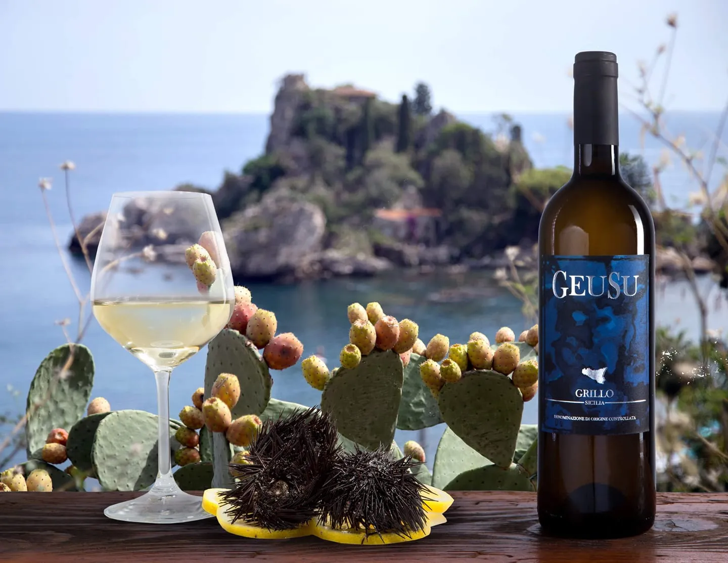Calice e bottiglia di Grillo Geusu con fichi d'India e ricci di mare davanti a Isola Bella, Taormina