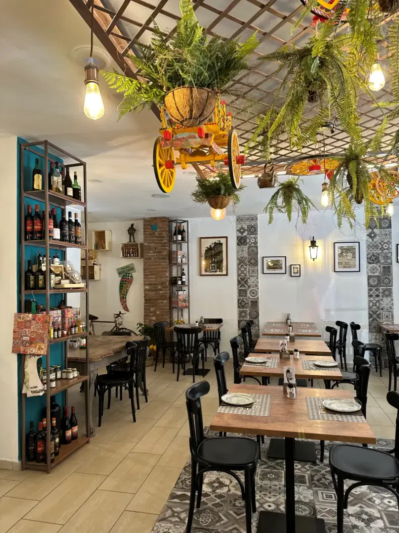 La sala di Vossìa Palermo: scaffali di vino, tavoli apparecchiati e il carretto siciliano appeso al soffitto