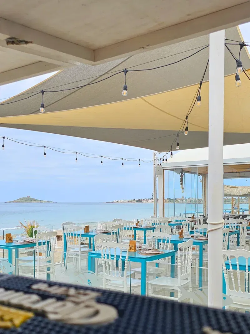 La terrazza coperta di Vossìa Ammare: le lampadine appese sopra i tavoli, la spiaggia e l'Isola delle Femmine sull'orizzonte