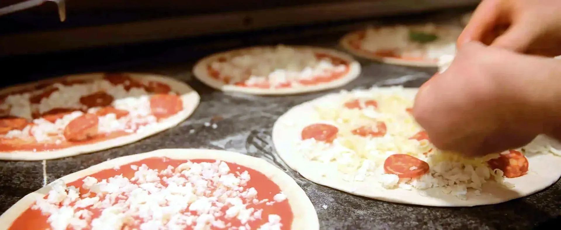 Il pizzaiolo condisce le basi delle pizze sul banco
