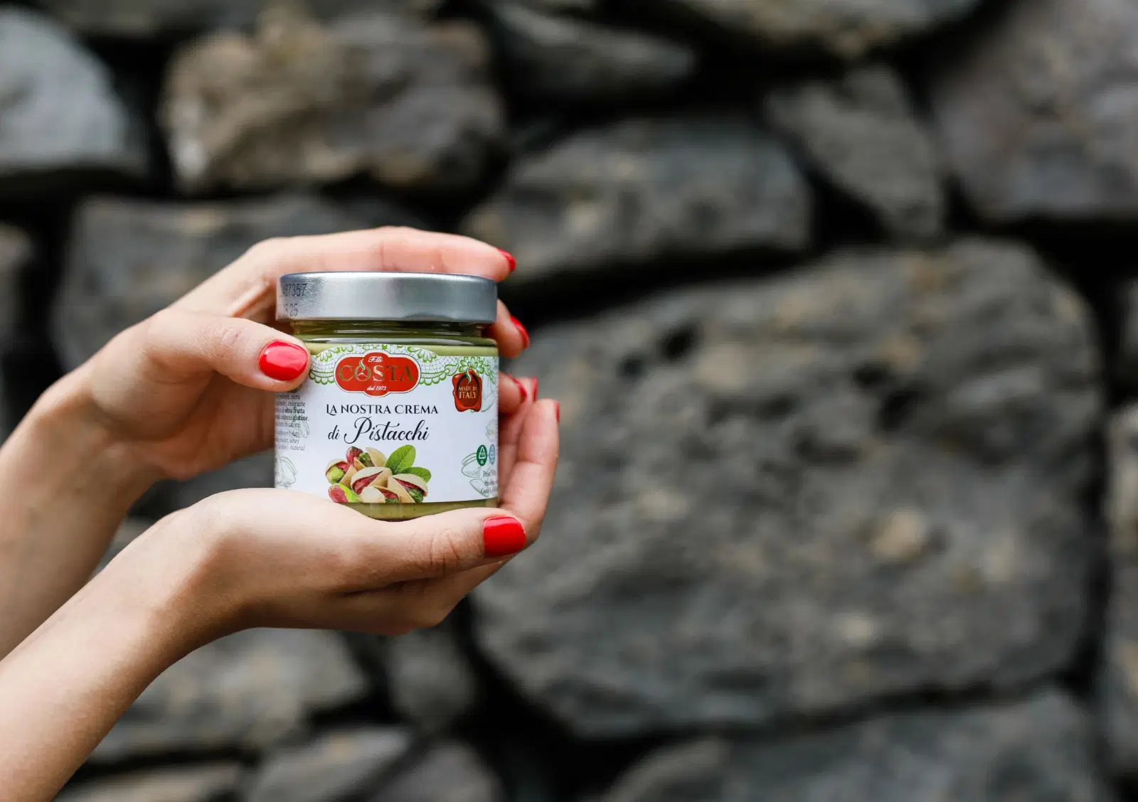 A jar of Costa cream held up against a wall of lava stone
