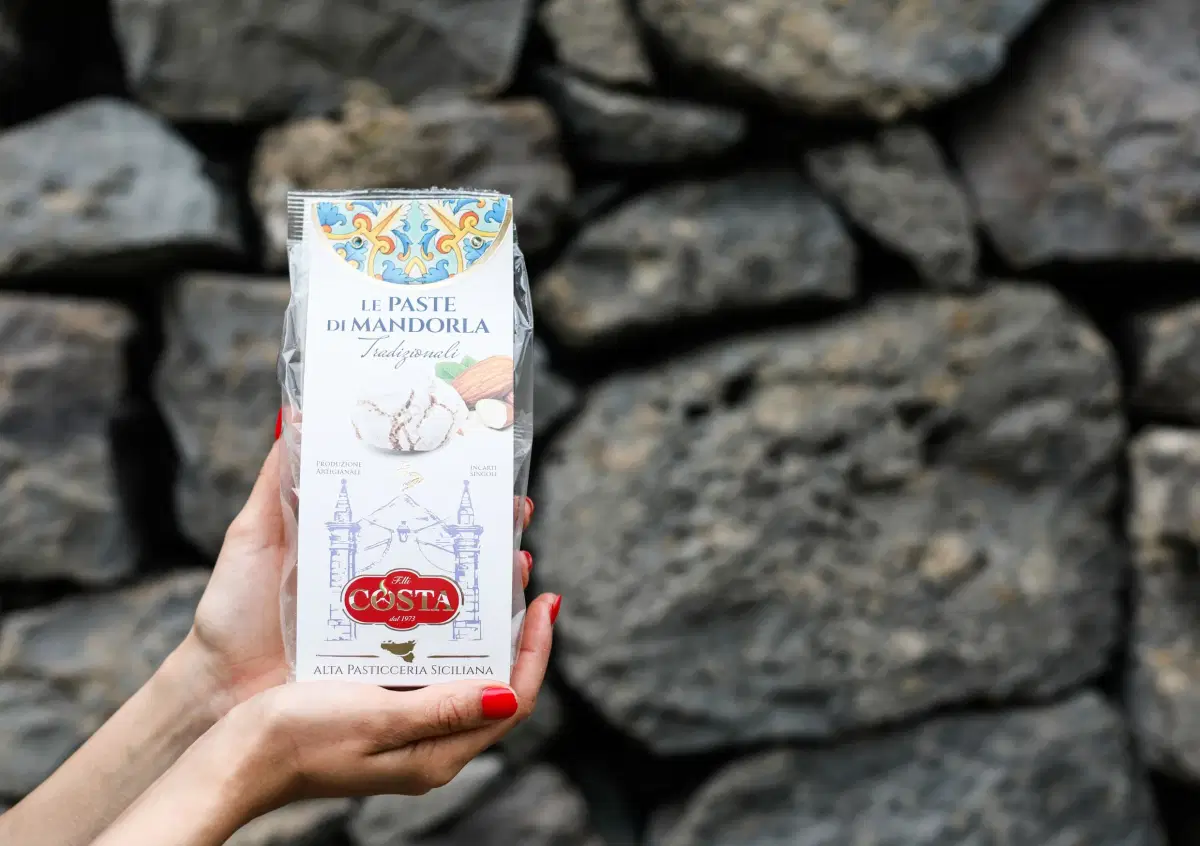 Un sacchetto di paste di mandorla tenuto in mano davanti a un muro di pietra lavica