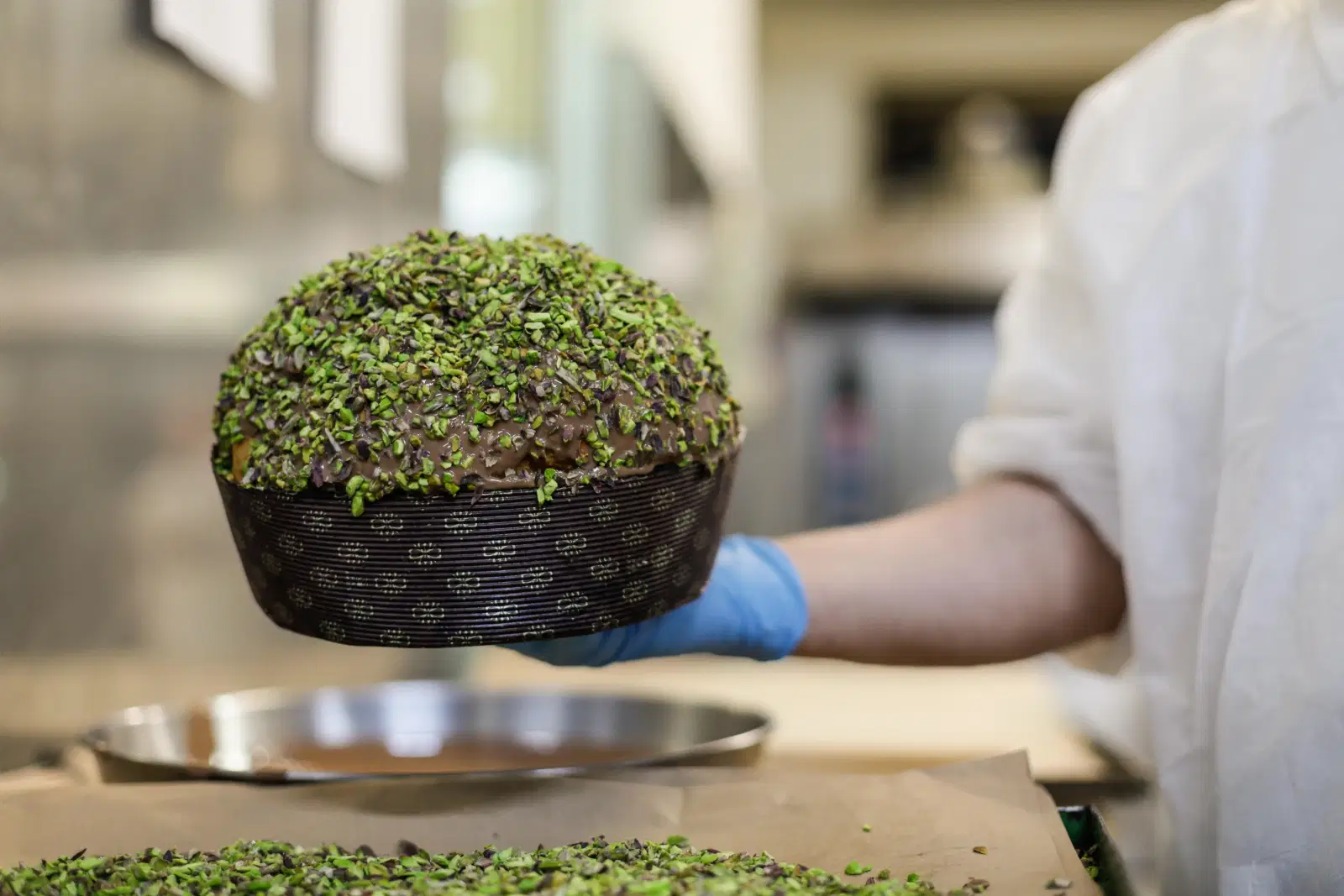 Un panettone coperto di granella di pistacchio, tenuto sopra il vassoio